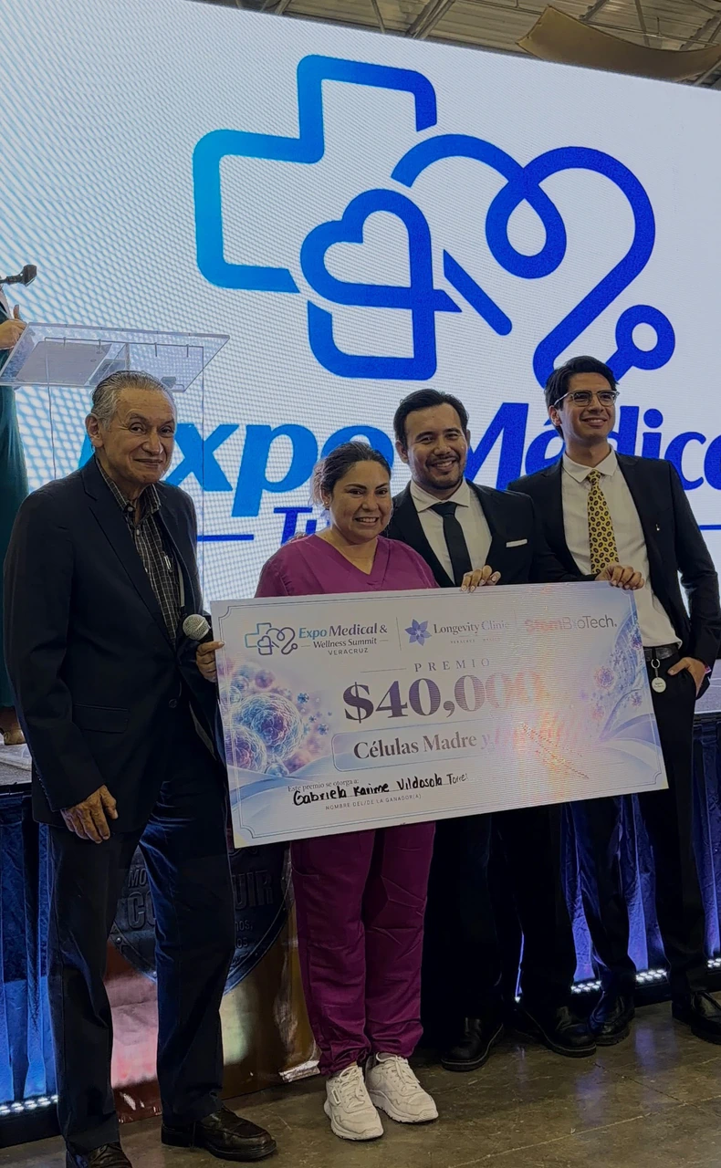 Entrega del premio de 40,000 pesos en terapia con células madre y exosomas: la ganadora sostiene el cheque junto al equipo de Longevity Clinic en el escenario de la expo