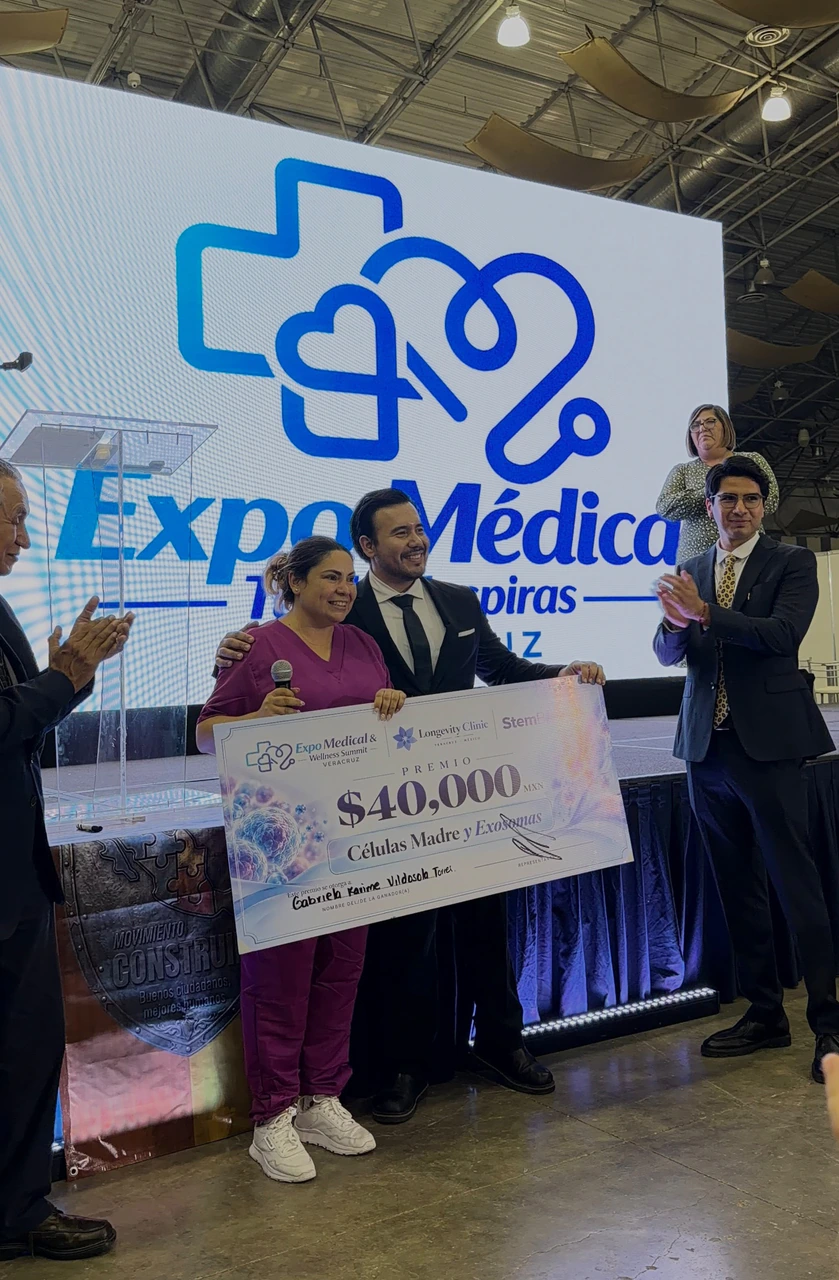 El público aplaude mientras la ganadora y el equipo de Longevity Clinic muestran el cheque del premio en el escenario