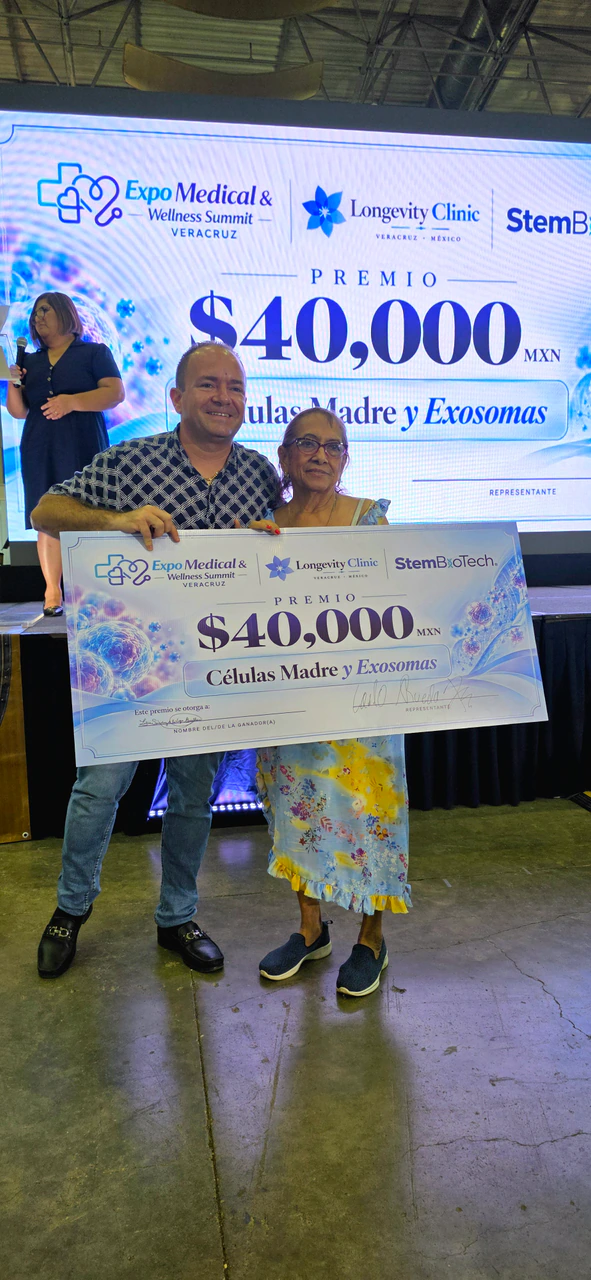 Dos personas ganadoras sostienen el cheque de 40,000 pesos frente a la pantalla del premio de Longevity Clinic y Stem BioTech
